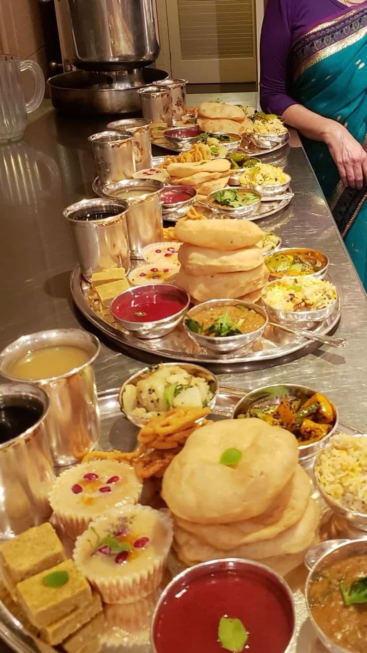 A long table of plates laden with puris, sweets, and curries