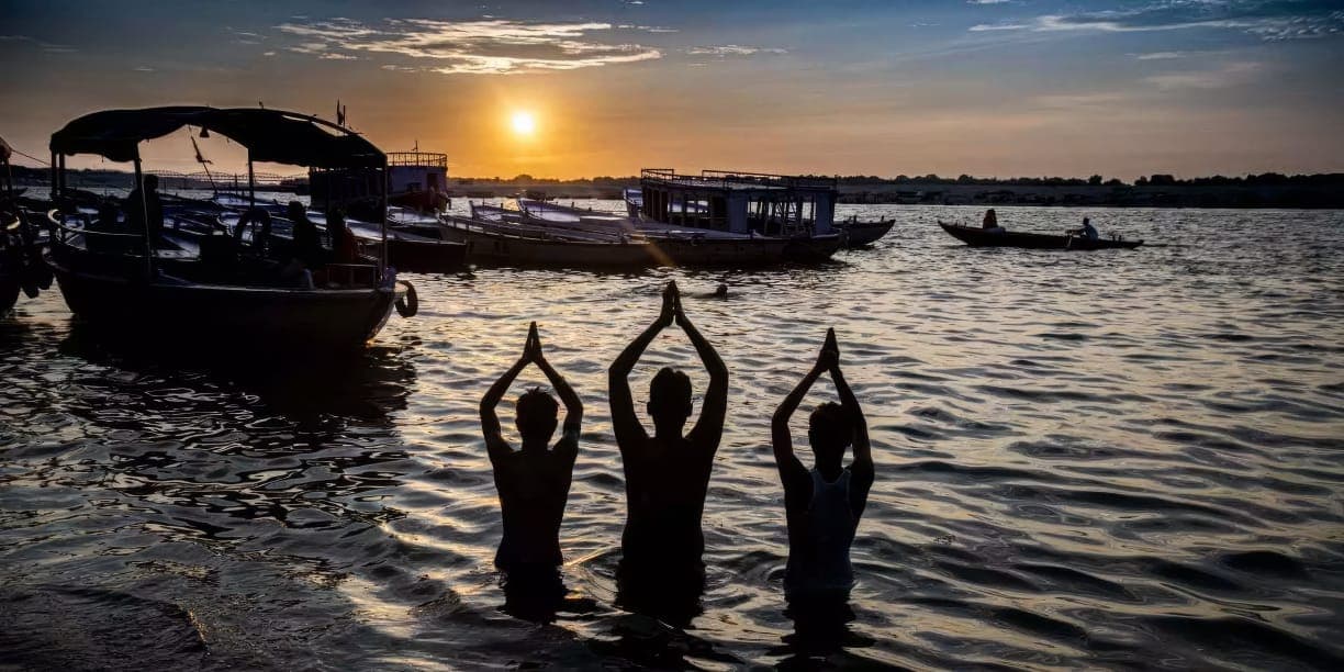 Three people standing in the river with hands joined overhead at sunrise